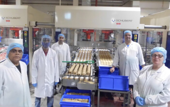 Five people wearing hair nets standing in a factory looking at the camera